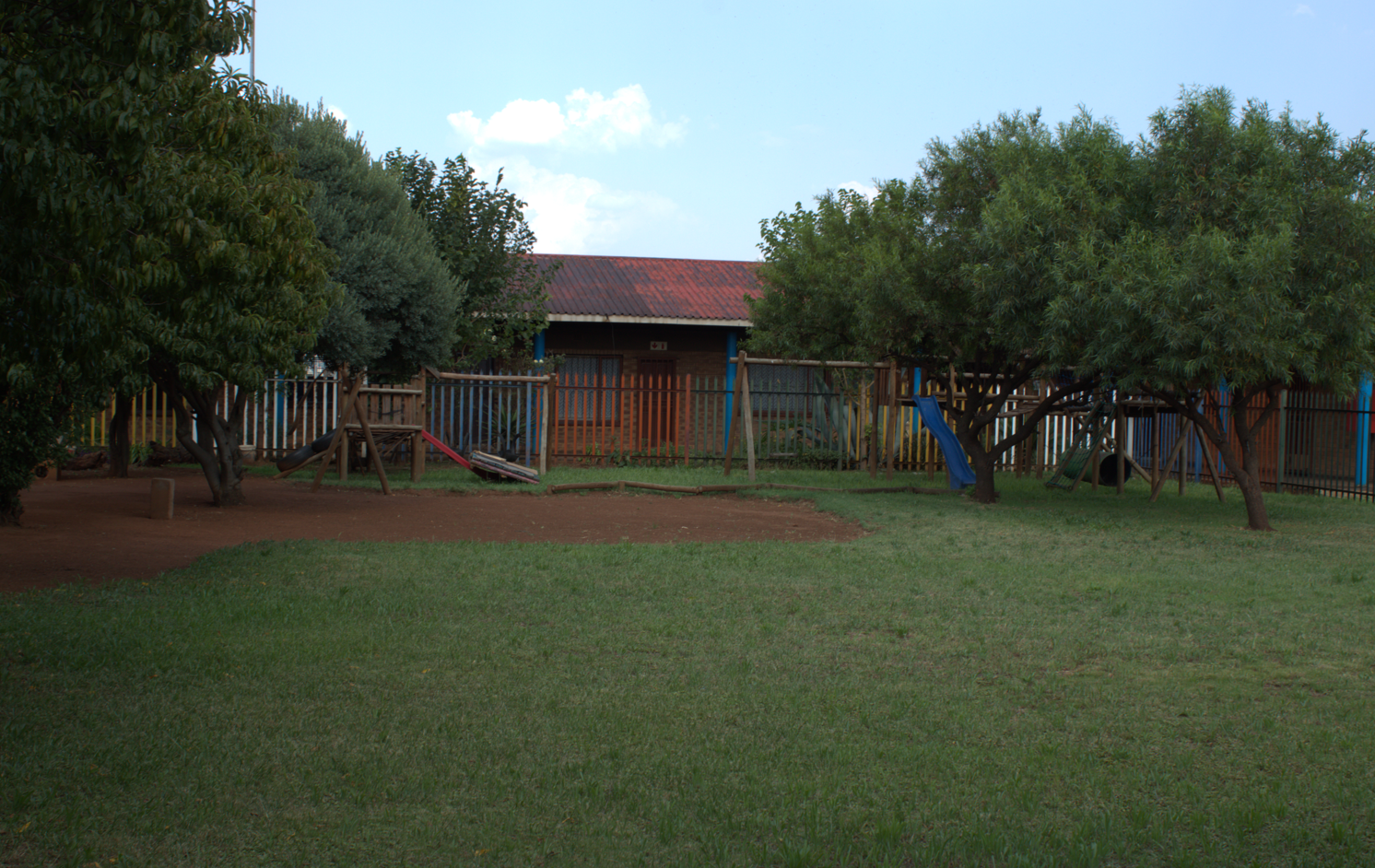 Katha Day Care's fenced outdoor Safe Park with trees and playground equipment